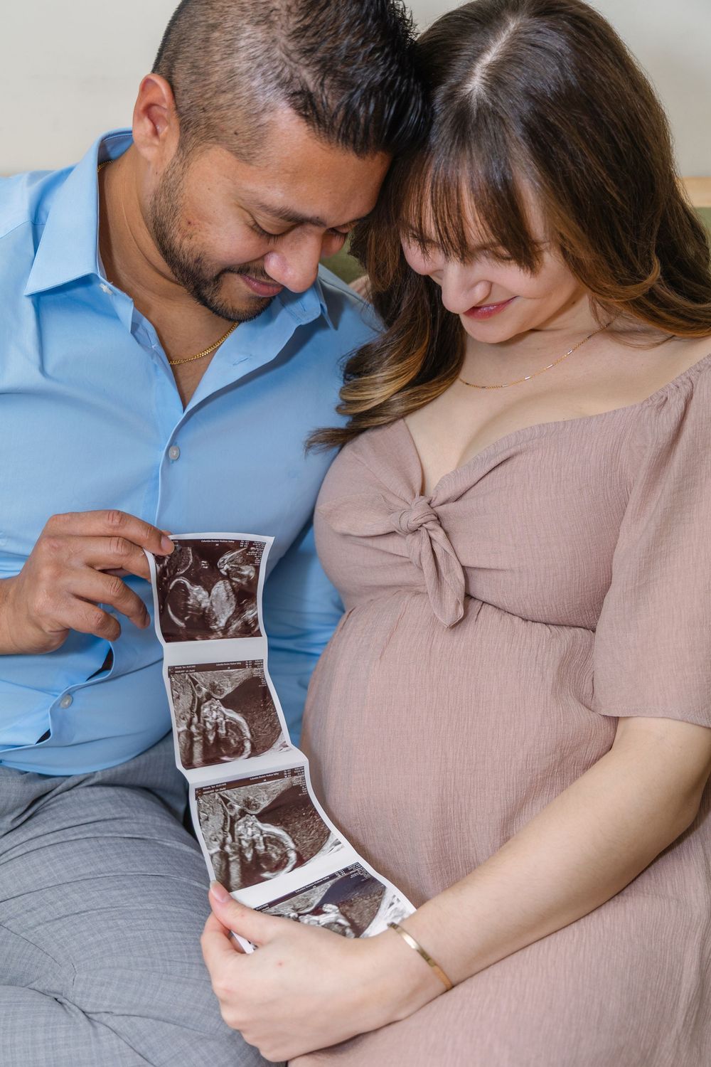 Expecting couple shares intimate moment while looking at ultrasound photos on couch together.