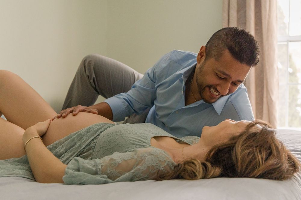 A couple lying together intimately on a bed in soft natural lighting.