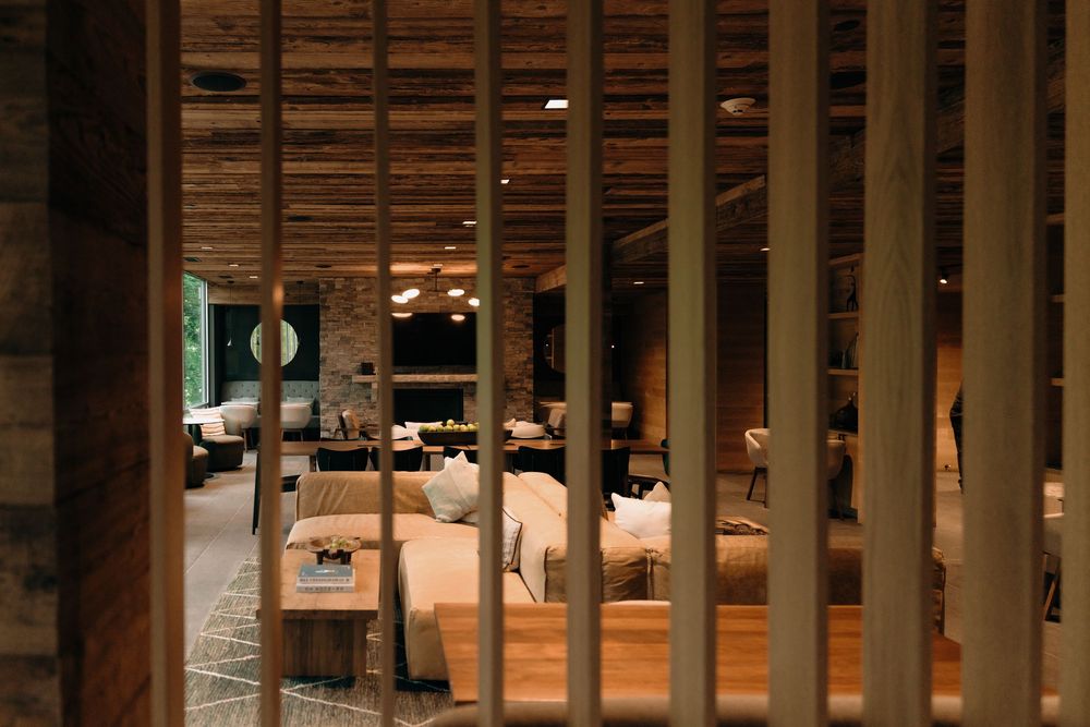 View through wooden slats into an elegant restaurant dining room with warm lighting and table settings.