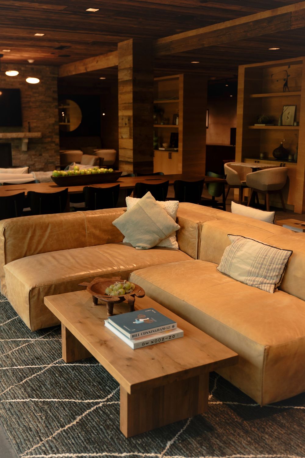 A cozy modern living space with tan leather sectional sofa, wooden coffee table, and built-in shelving against brick walls.