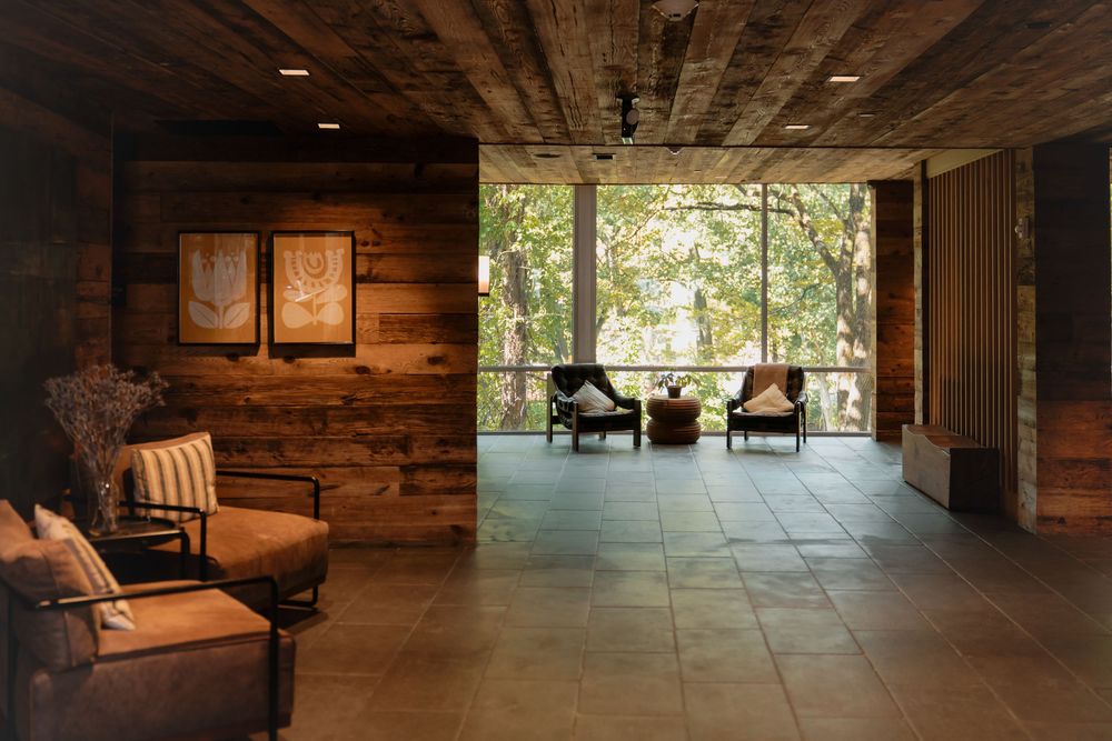 A rustic wooden cabin interior with stone flooring and natural light streaming through large windows.