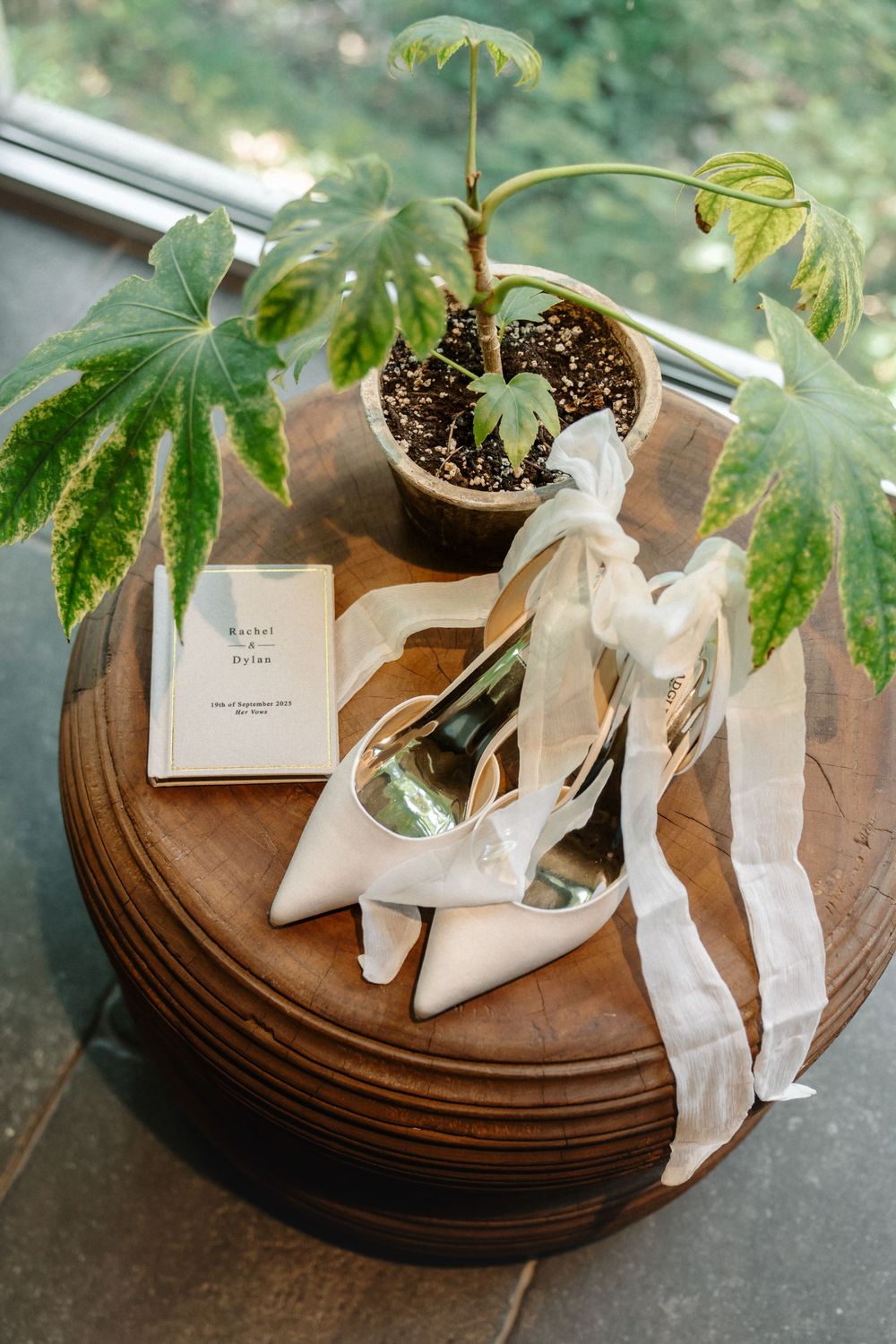 Elegant ivory wedding shoes displayed with potted plants on wooden coasters in a romantic garden setting.
