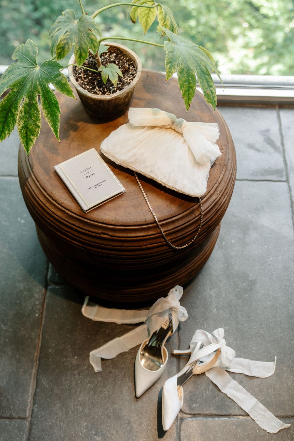 Elegant bridal accessories including white shoes with ribbons and a potted plant arranged on a round wooden table.
