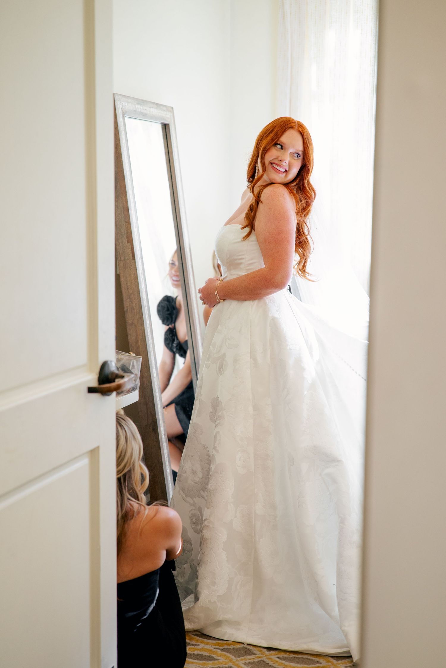 A bride with her flowing white wedding dress with delicate lace details spreads across lush green grass in outdoor bridal portraits.