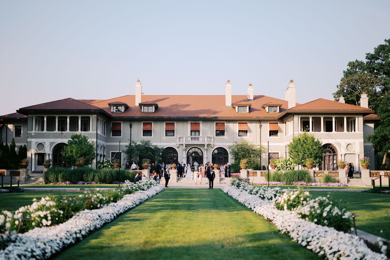 A panoramic view of a Mediterranean-style mansion with a grand lawn and white chairs set up for an outdoor event.