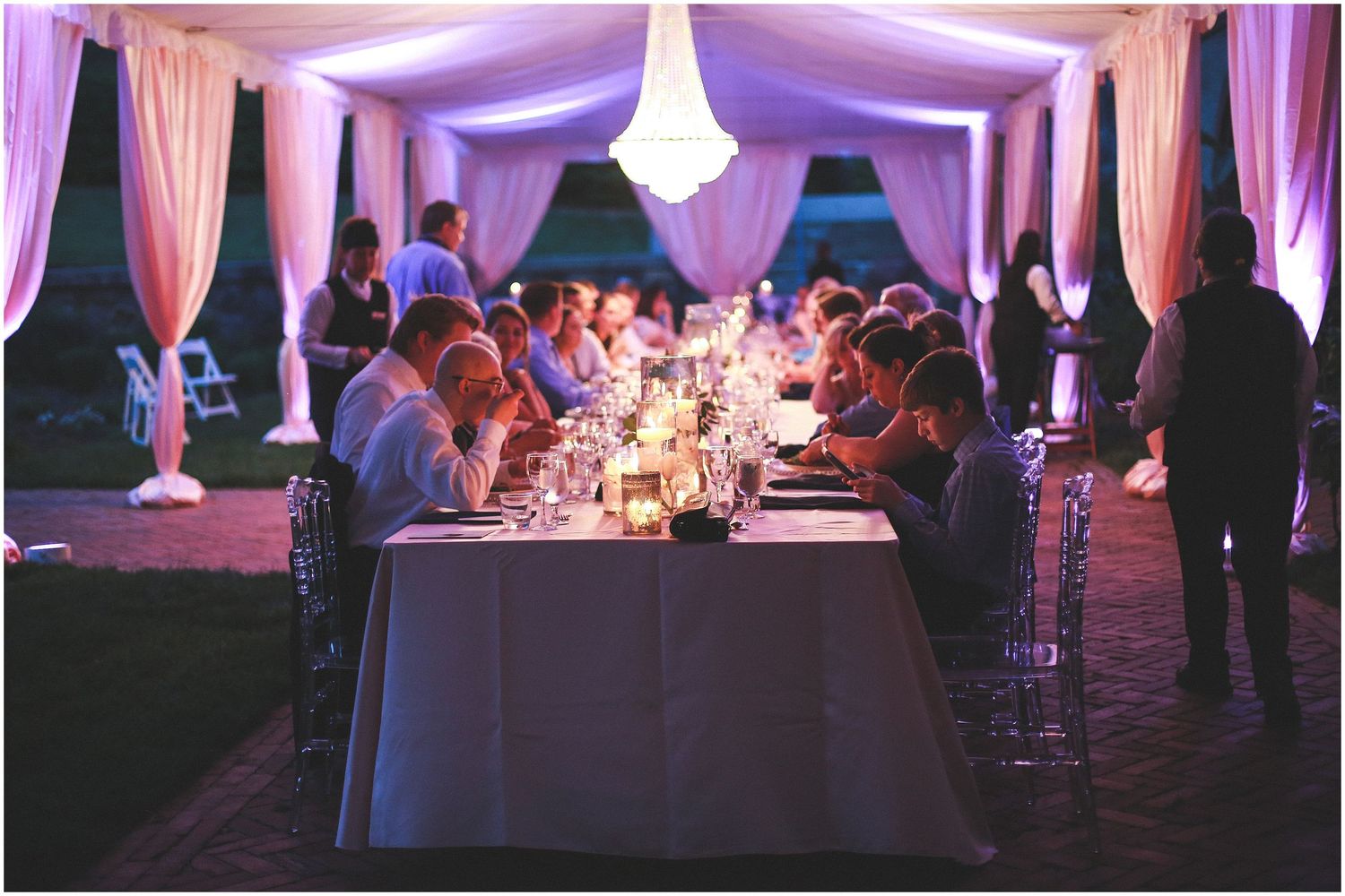 Wedding reception venue decorated in pink lighting with guests seated at round tables for dinner service.