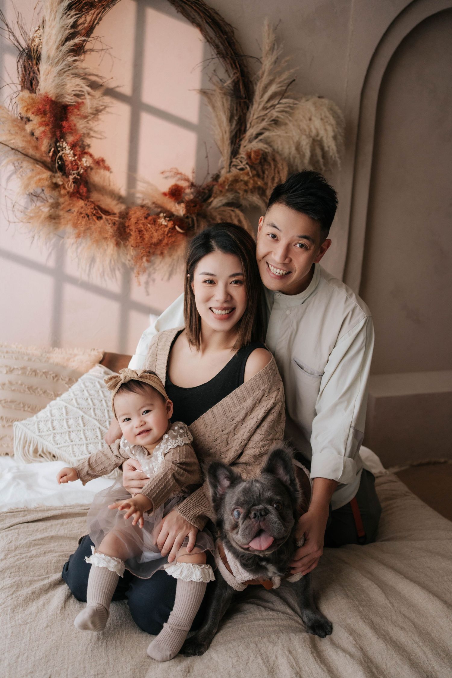 Happy Asian family with baby girl and French Bulldog posing in boho-styled photo studio with dried floral decor.幸福的亞洲家庭帶著女嬰和法國鬥牛犬在以乾燥花裝飾的