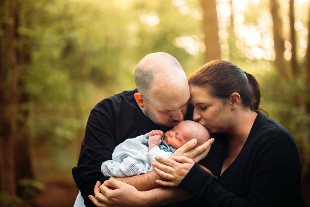 Intimate family portrait in sunlit forest setting with soft golden light.