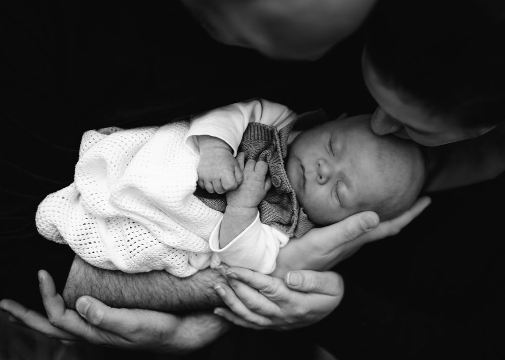 A tender black and white portrait of a newborn being cradled in gentle hands.