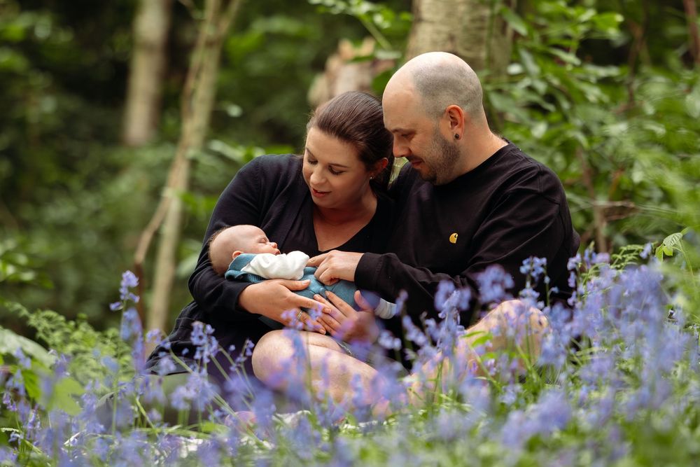 Tender family moment captured among blooming bluebells in woodland setting.