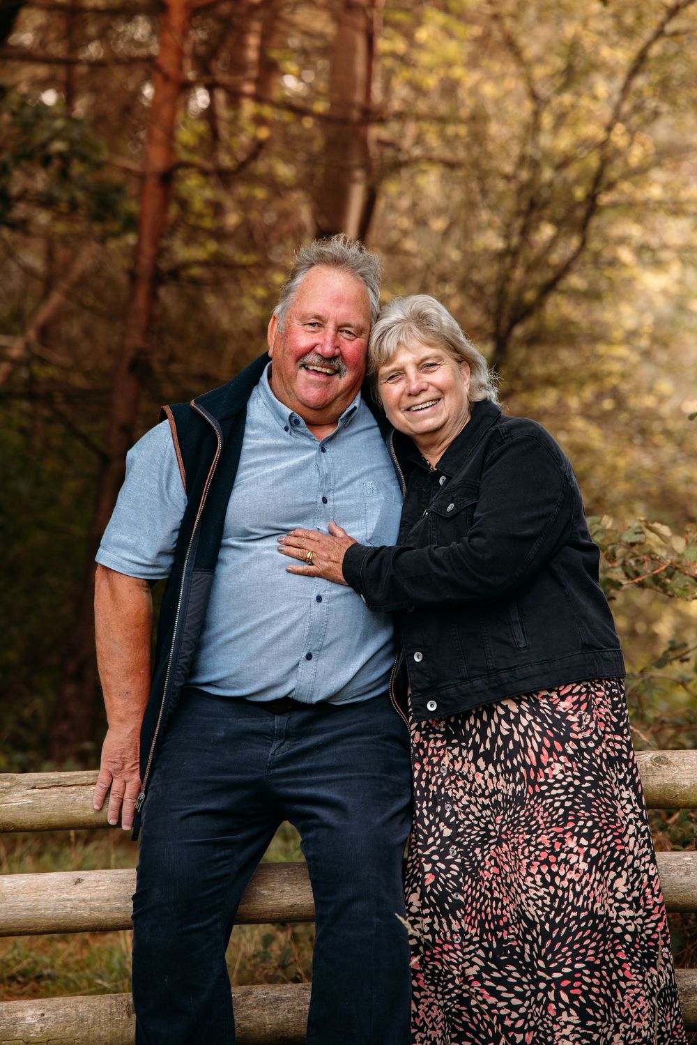 Couple sharing a joyful moment together on wooden fence in autumn forest.