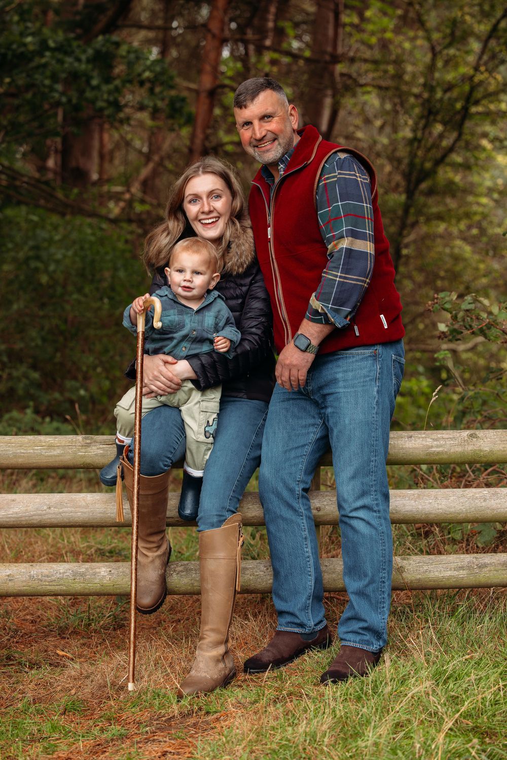 Family members lean against wooden fence in casual outdoor setting.