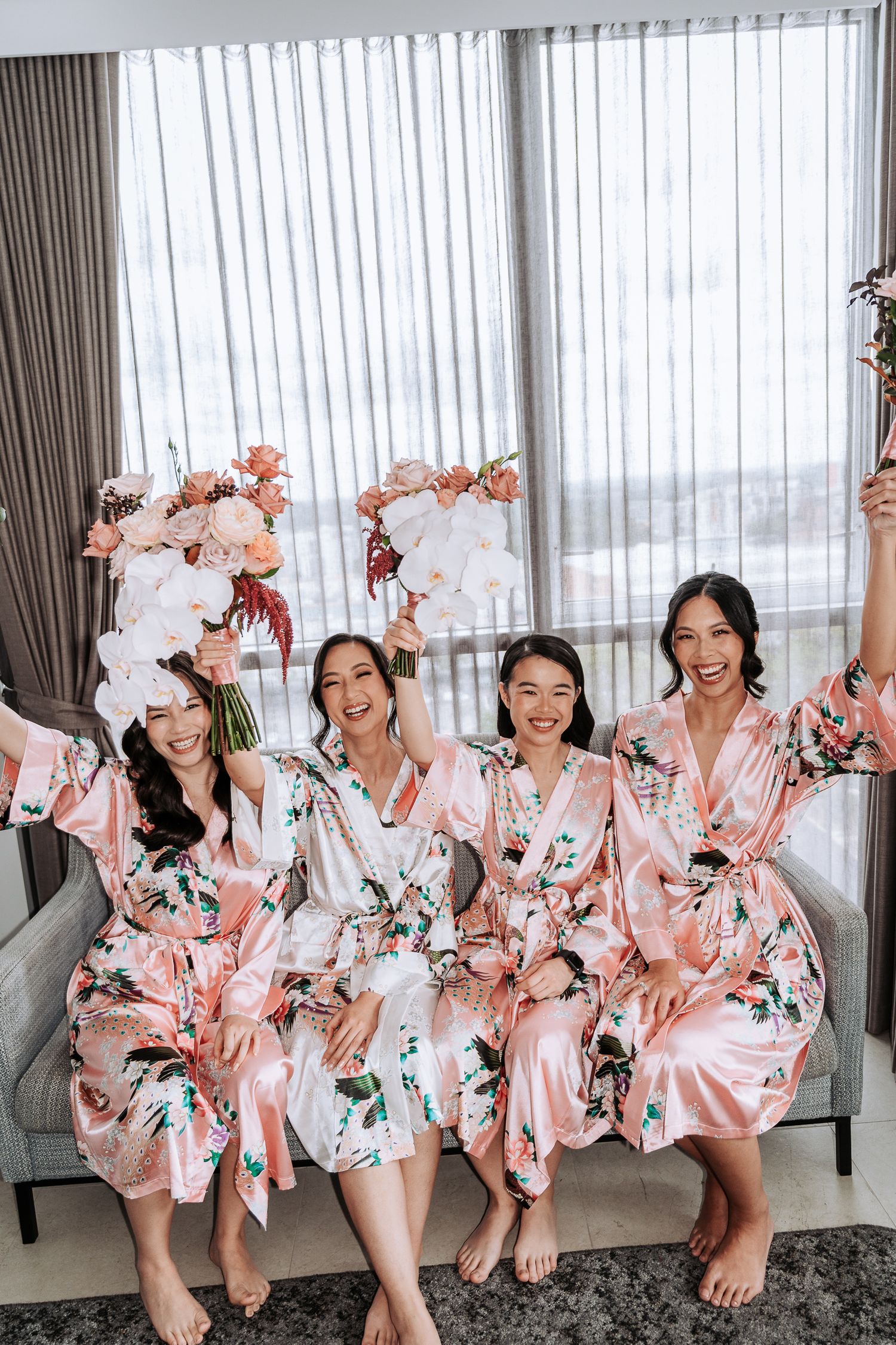 A group wearing matching pink floral robes pose playfully together in a bright room with sheer curtains.