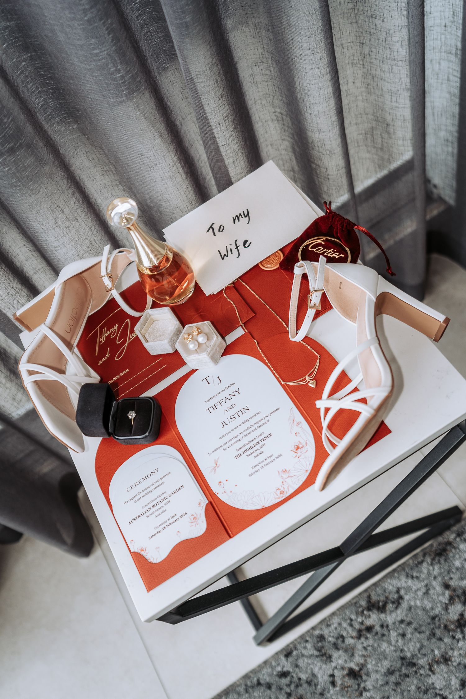 Red and white wedding invitation cards with elegant design lay arranged in a sequence on a gray surface.