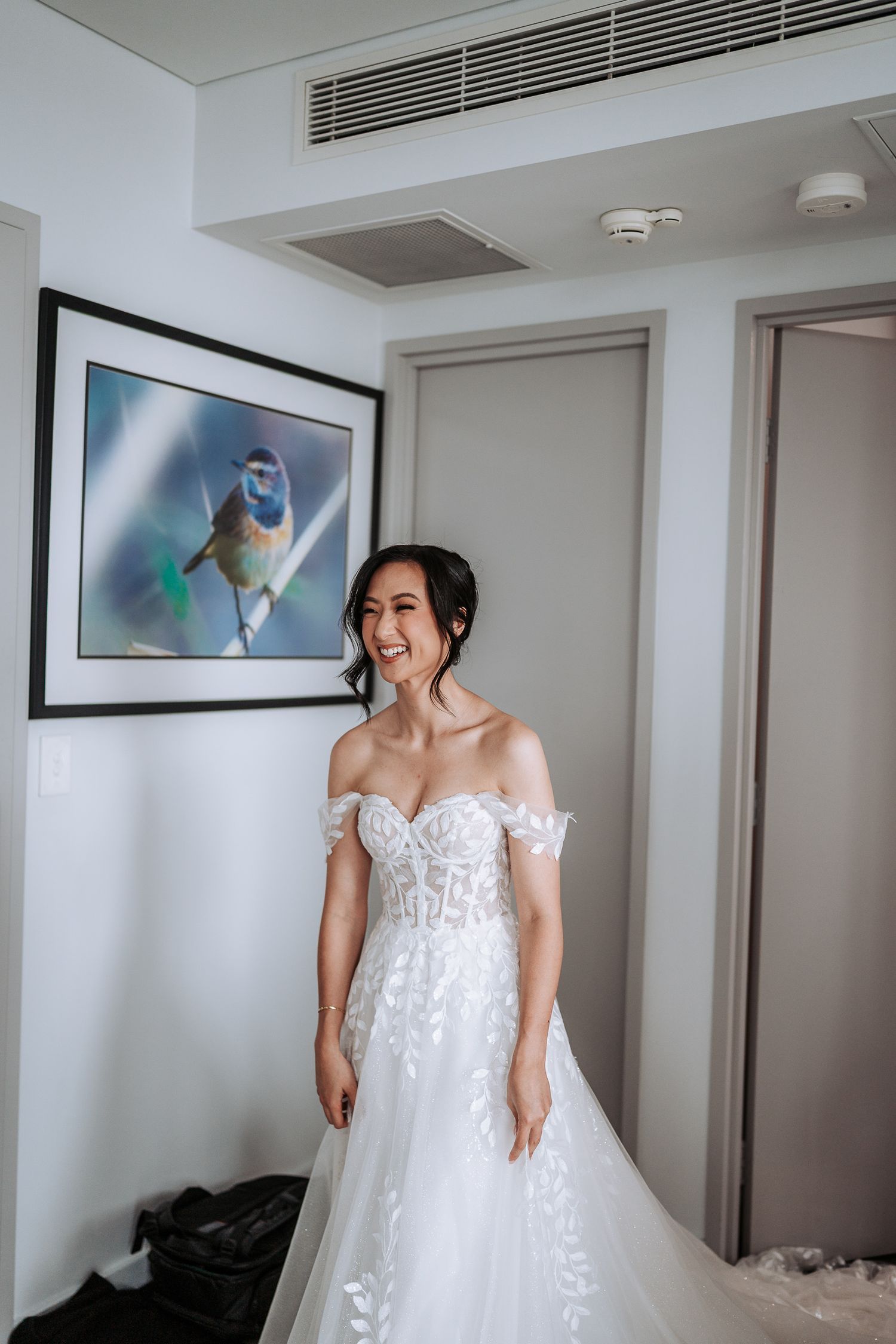 A series of four photos showing a bride in a white lace wedding dress getting ready in a bright hotel room.