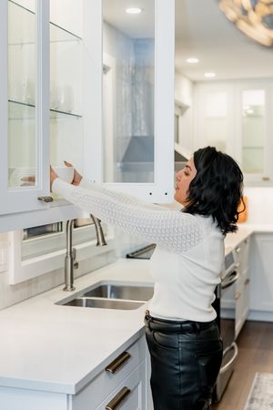A sequence of photos showing someone reaching up to grab items from high white cabinets in a modern kitchen.
