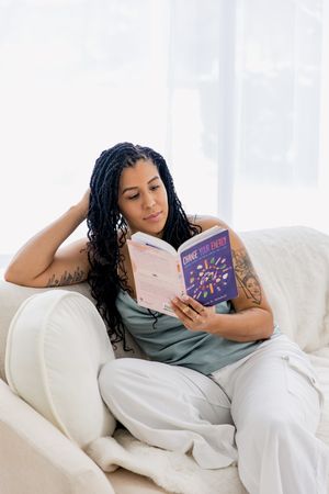 Someone relaxes on a white couch while reading a book in a bright, airy room.