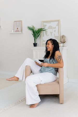 A reader lounges comfortably in a minimalist room with white decor and small potted plants.