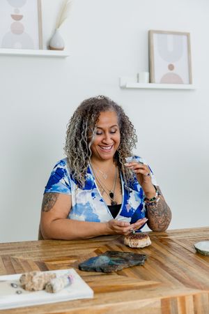 A person with curly gray hair sits at a wooden table looking at their phone while enjoying dessert.