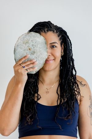 Person with long braided hair wearing a navy blue top holds a large white crystal or mineral specimen over part of their face.