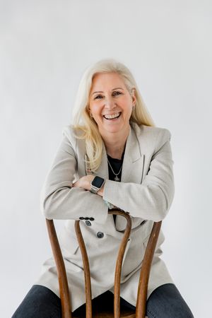 Professional studio portrait of someone wearing a light colored blazer and dark top posing playfully against a white background.
