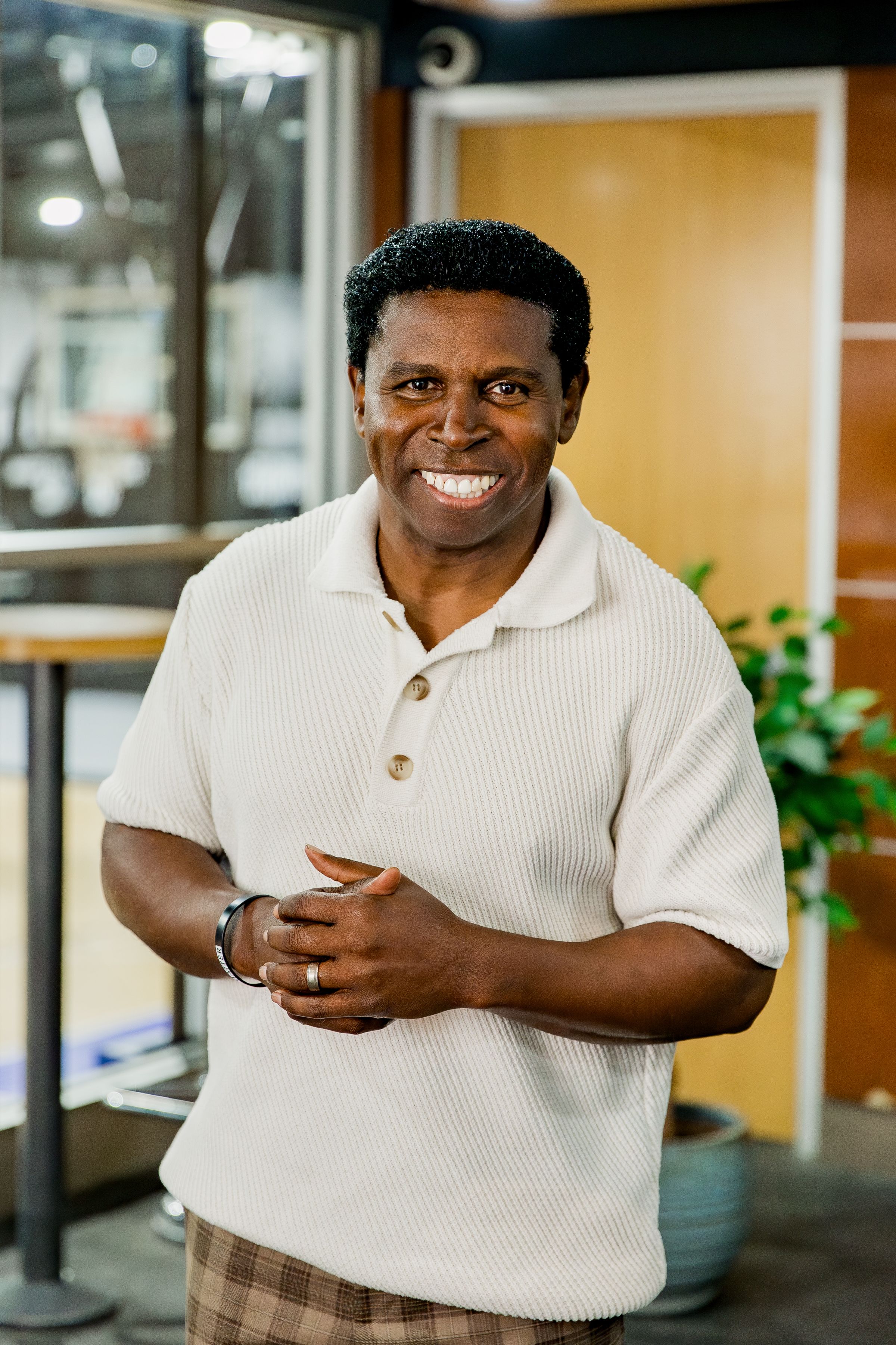 Pinball Clemons wearing a white knit sweater smiles warmly while standing in an athletic training centre.