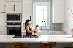 Modern white kitchen with dark wood island features sleek cabinets, stainless appliances, and natural light from windows.