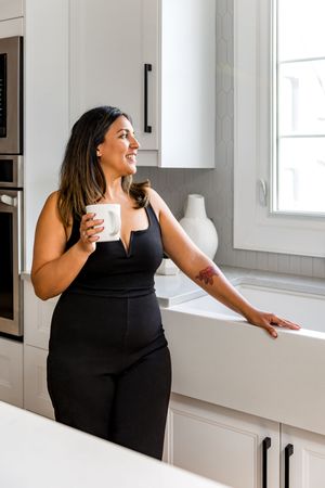 Woman in black sleeveless top laughing joyfully in bright modern kitchen interior.