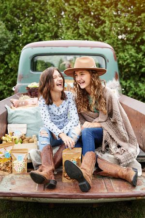 Two friends share laughter while relaxing in the back of a vintage pickup truck on an autumn afternoon.