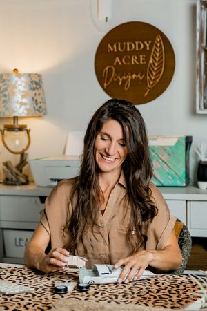 Woman writing and smiling at desk with leopard print surface and decorative wall signs in background.