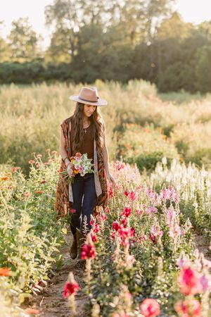 A person in a brown coat and hat walks through a garden of pink and white flowers during golden hour sunset.