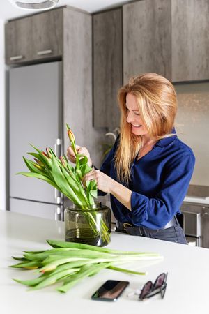 A person in a blue sweater arranges fresh tulips in a bright modern kitchen setting.