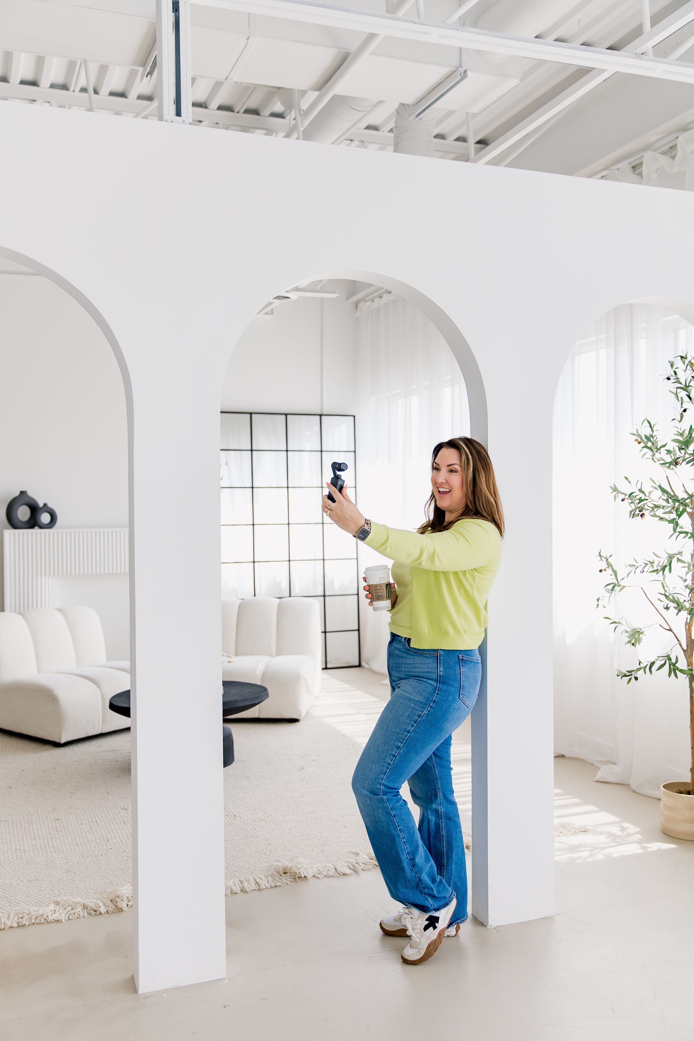 Person in yellow top and blue jeans poses in sequence against white studio walls and columns.