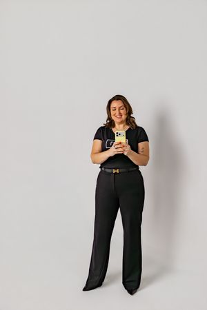 Someone wearing a black t-shirt and wide-leg pants stands against a white background while looking at their phone.