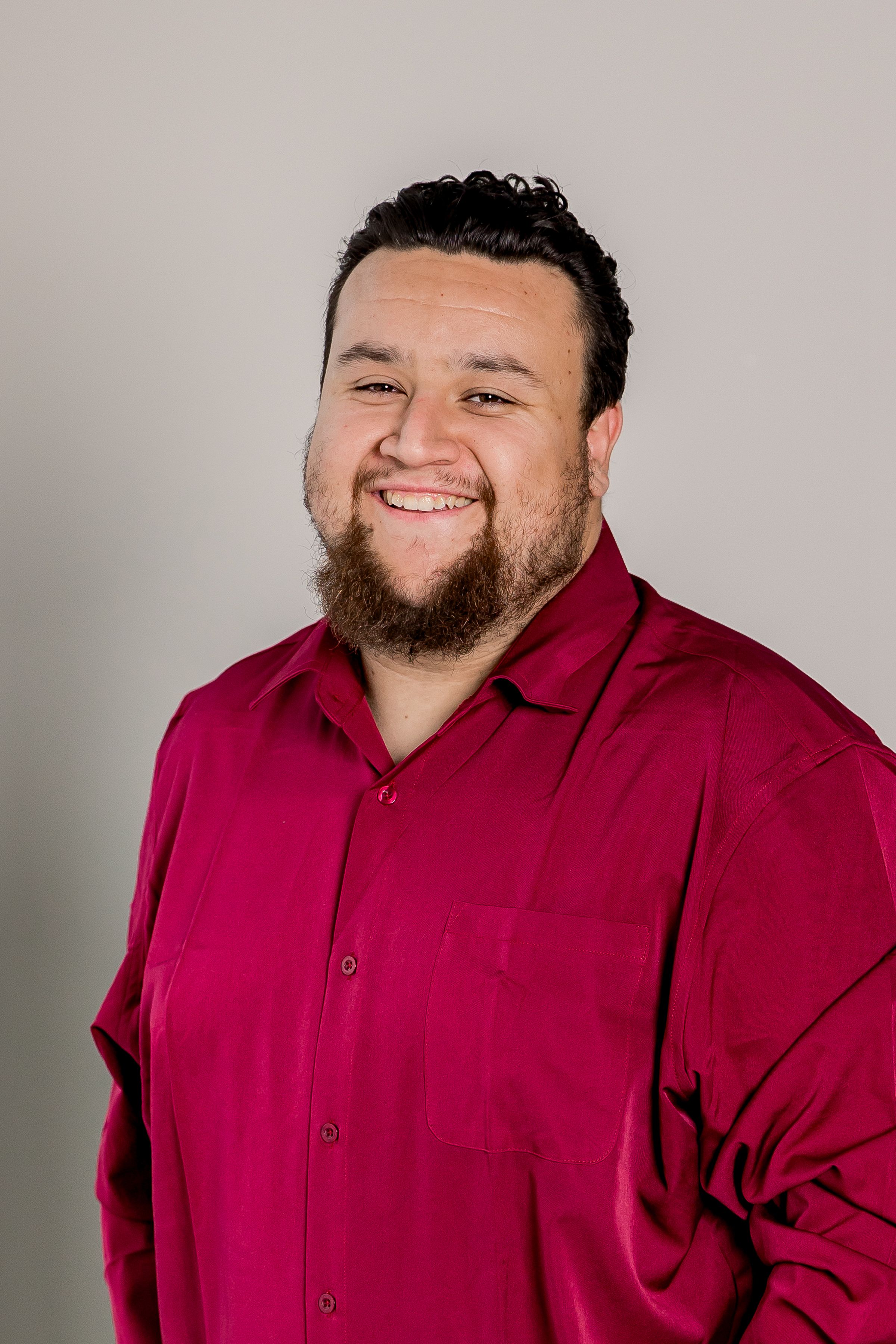 Professional headshot of a person in a burgundy button-down shirt smiling warmly against a light gray background.