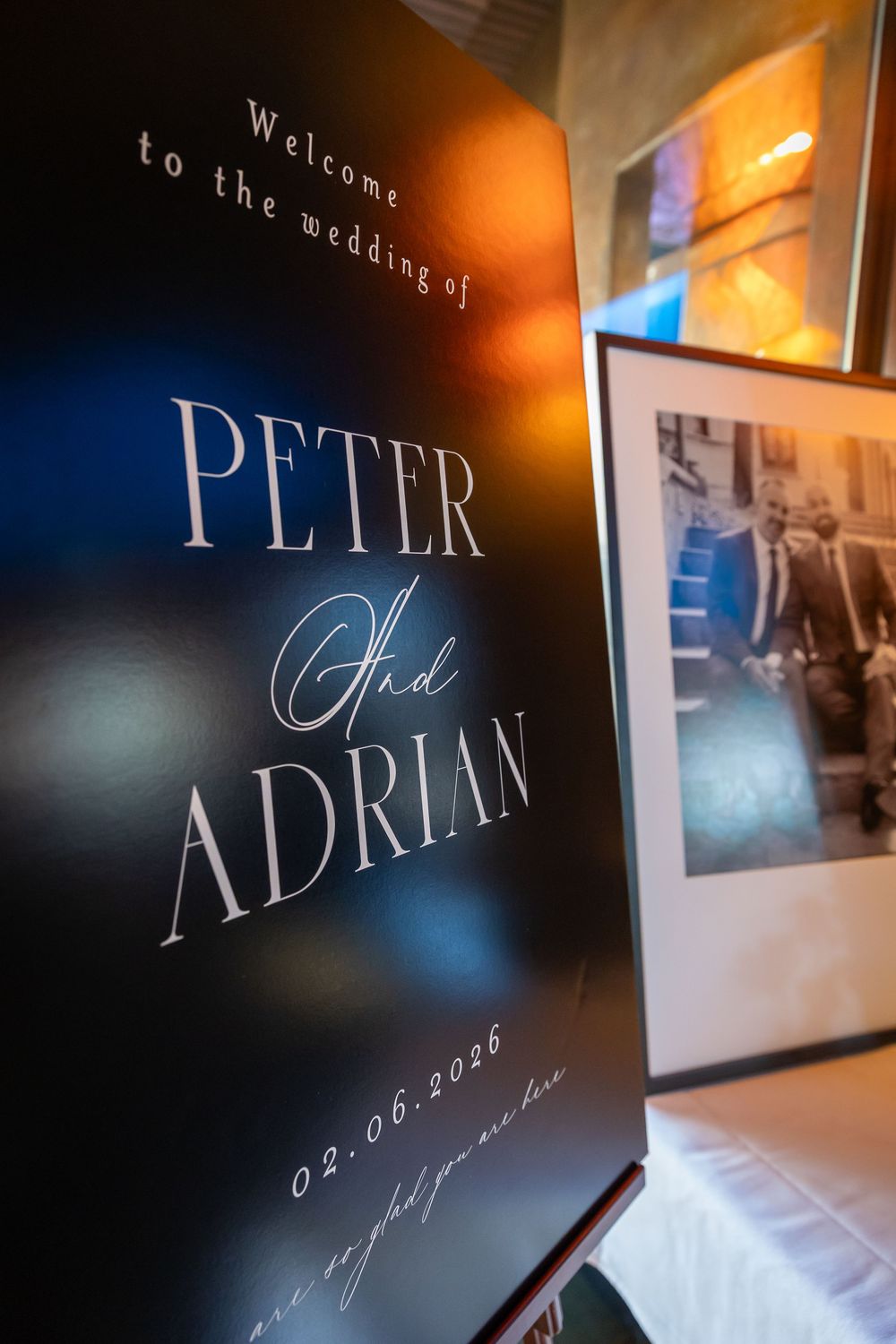 Elegant wedding signage displays 'PETER ADRIAN' in stylish typography against a dark background with soft lighting.