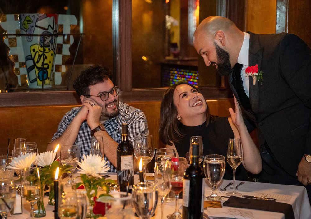 Diners share a lighthearted moment with server at an elegant restaurant table decorated with flowers and wine glasses.