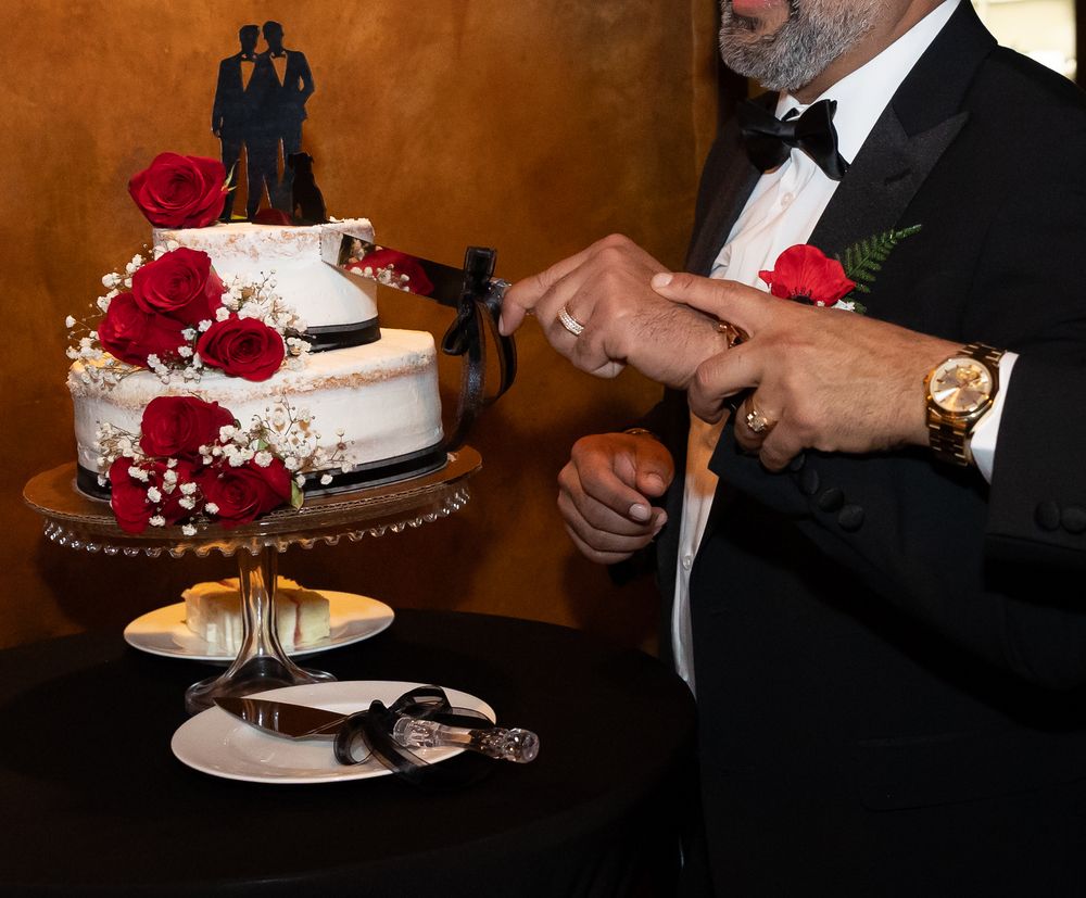 A wedding cake decorated with red roses is cut by the newlyweds during their reception celebration.