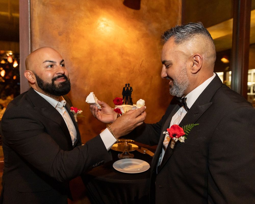 Two men in formal attire embrace warmly at an indoor event with warm lighting and elegant decor.