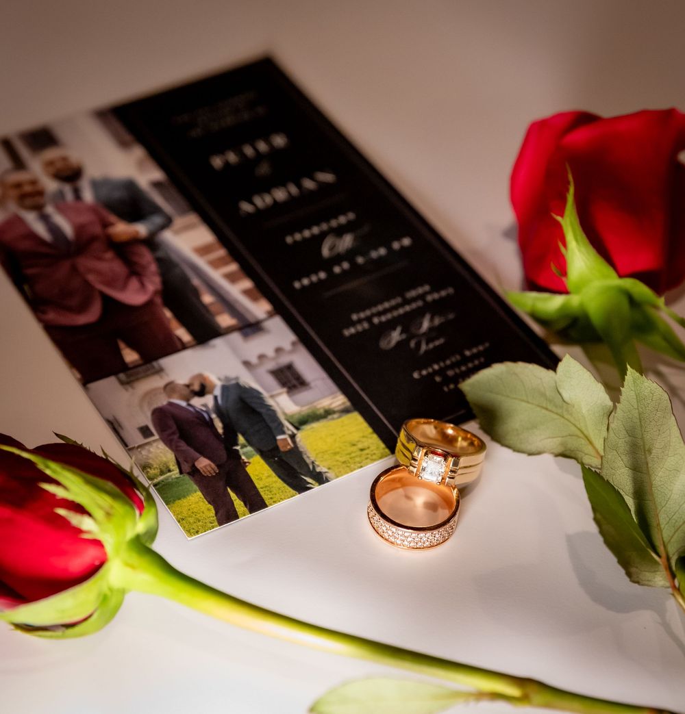 Wedding rings rest elegantly on black invitation cards with red roses adding romantic accents.