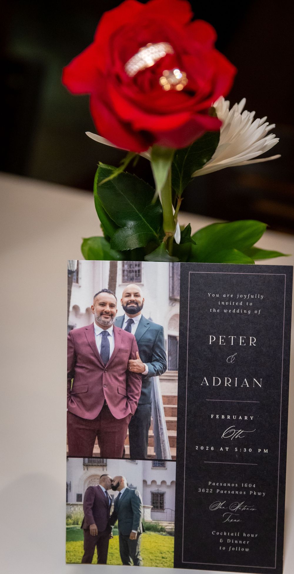 Wedding invitation with red rose and white daisy on top, showing elegant black and burgundy design with floral accents.