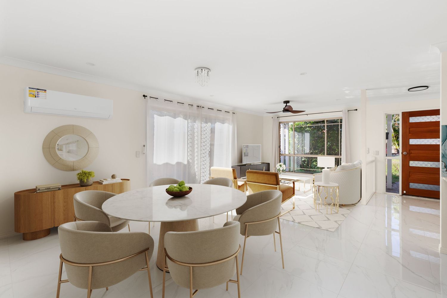 Bright open-plan dining and living area with round marble table and ceiling fan.