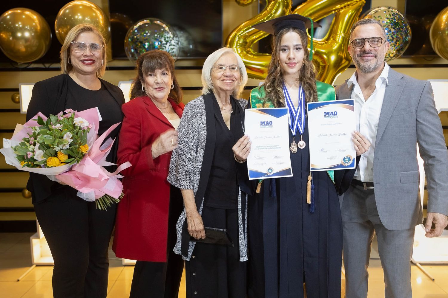 Award recipients stand together holding certificates and flowers during a recognition ceremony.