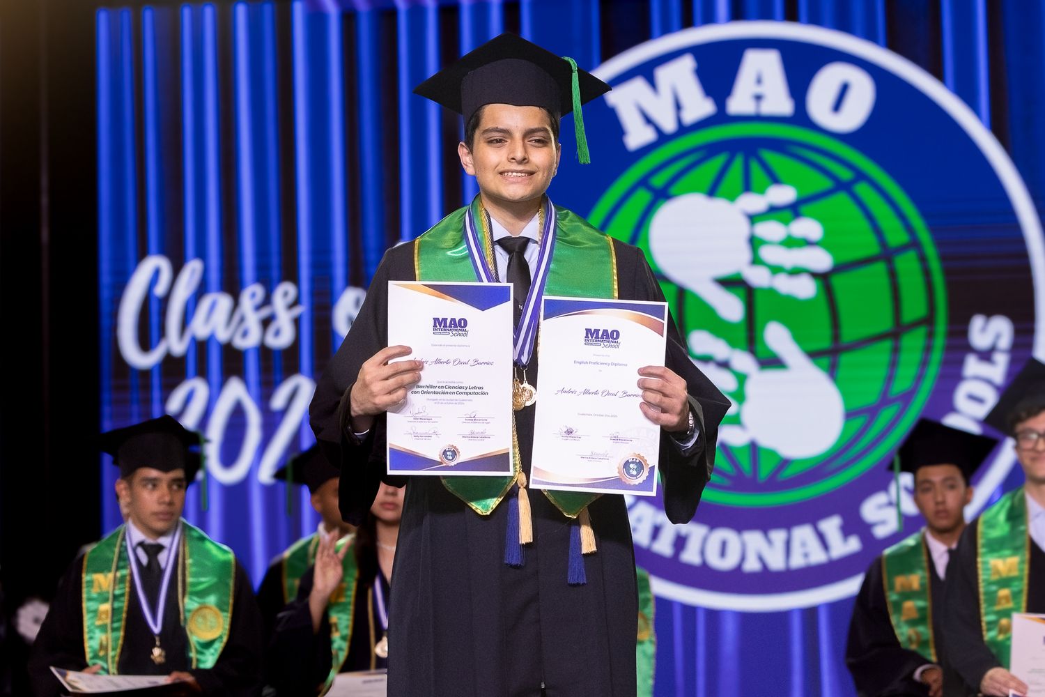 Spelling bee contestants stand on stage at the Scripps National Spelling Bee competition holding certificates and trophies.