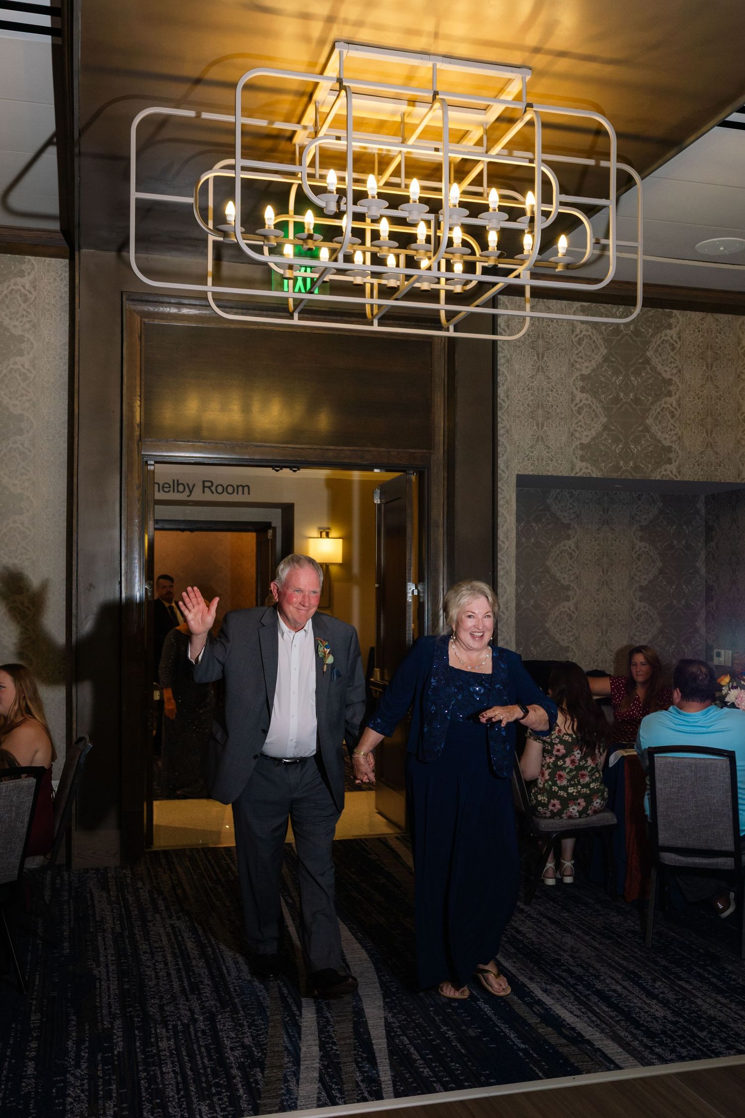Guests dancing under a modern geometric chandelier at an elegant event venue with patterned wallpaper.