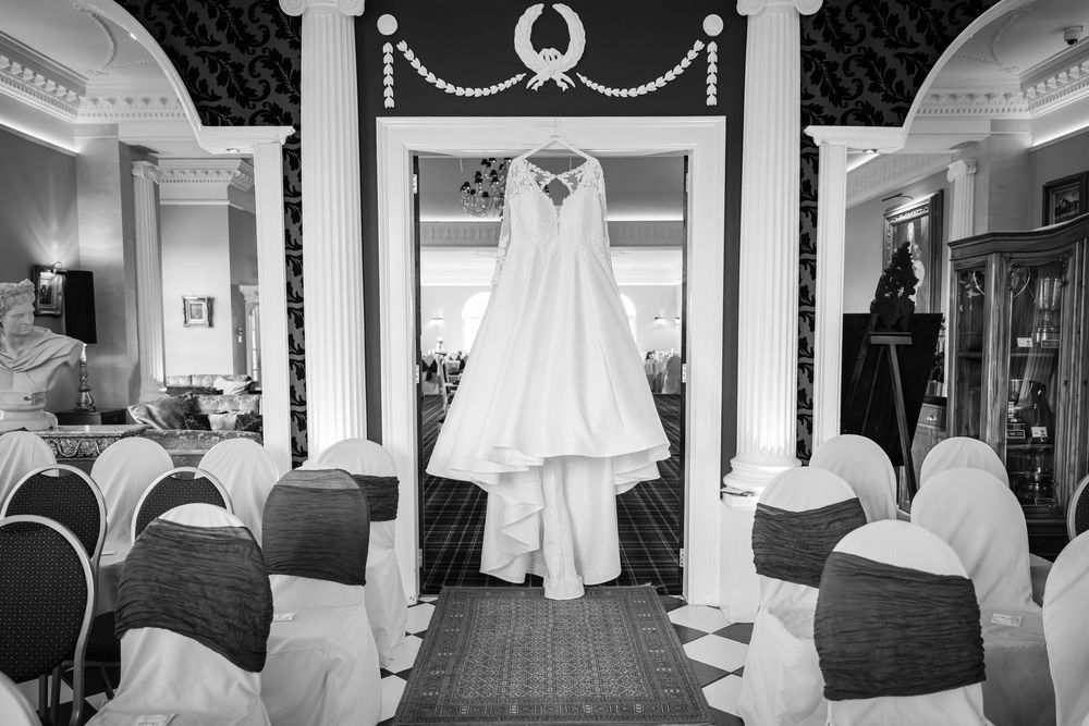 A series of black and white photos showing wedding dress preparations and details in an elegant venue hallway.