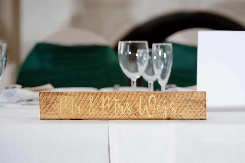 Elegant white wedding cake with teal ribbon and gold accents displayed on a rustic wooden table setting.