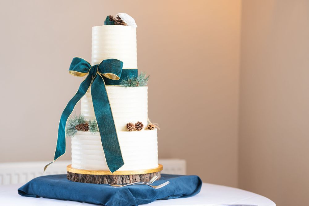 Modern white wedding cake adorned with a teal bow and gold trim on a navy blue tablecloth.