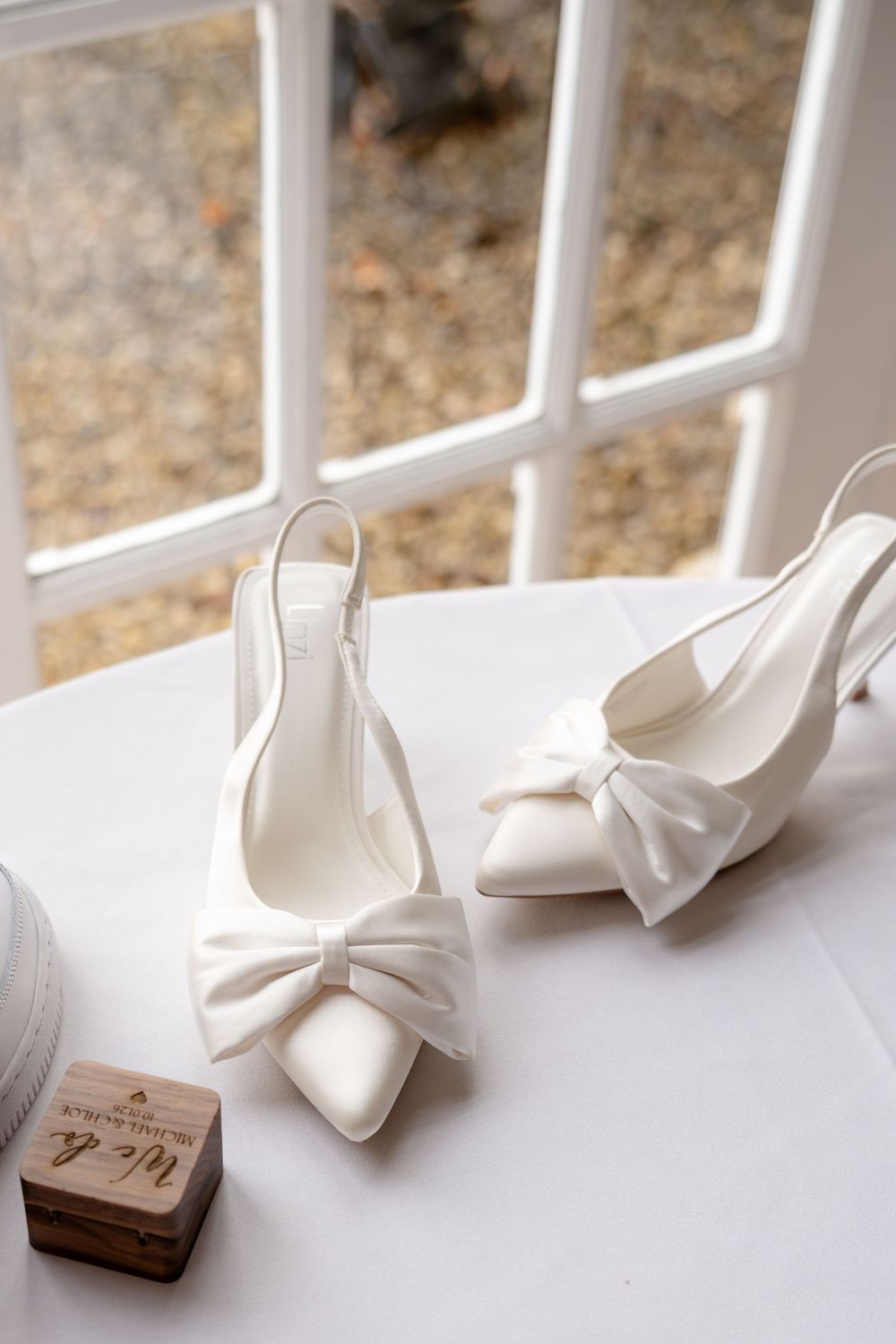White satin wedding shoes displayed in a row against a white windowsill with natural light.