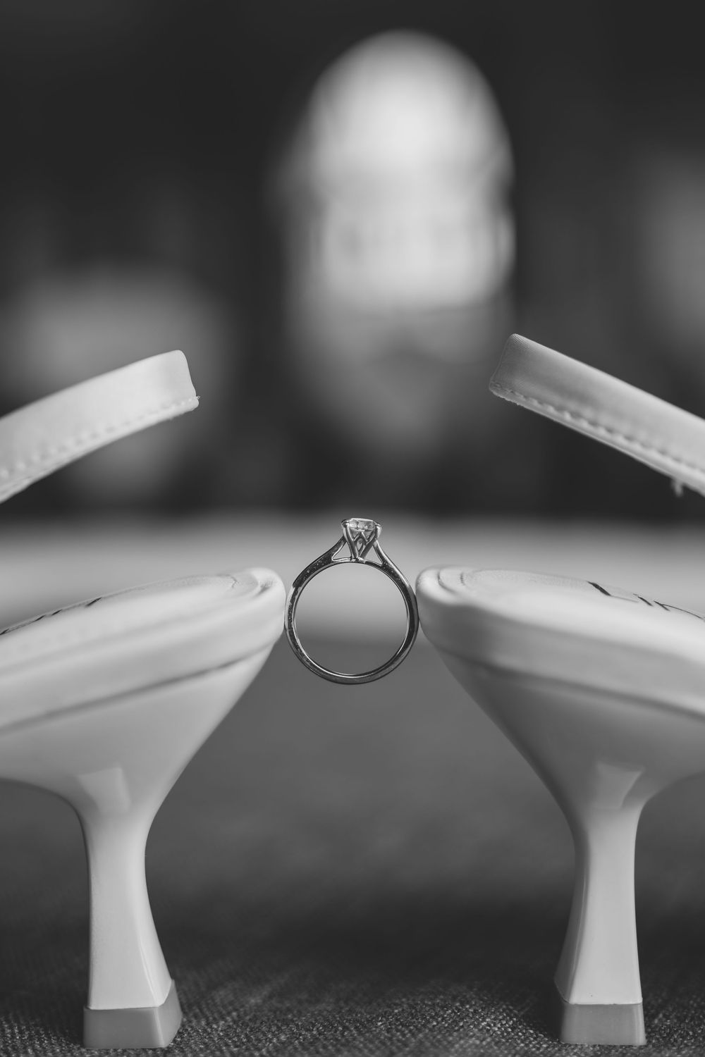 Diamond engagement ring balanced artistically between two white high heel shoes in black and white.